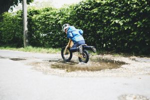 Enfant avec casque et veste de pluie roulant à vélo dans une flaque